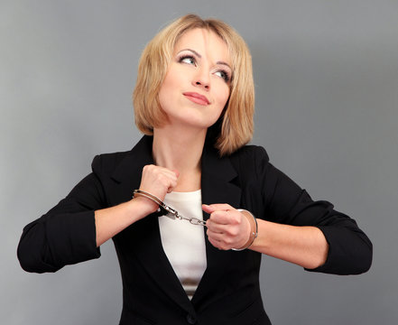 Young beautiful business woman in handcuffs on grey background