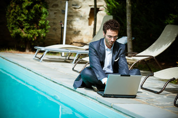 Young Businessman with Computer next to Swimming Pool