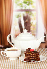 Teapot, cup of tea and delicious cake on window background