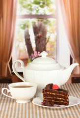 Teapot, cup of tea and delicious cake on window background