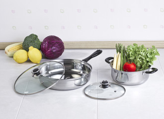 Set of stainless pot and pan with glass lids and vegetables