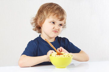 Little cute blonde boy refuses to eat a porridge