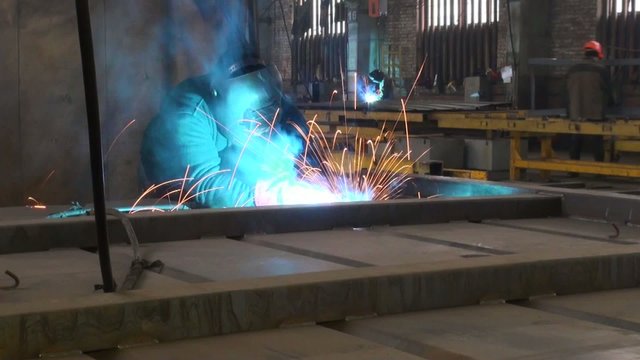 blue sparks fly from welding, people work