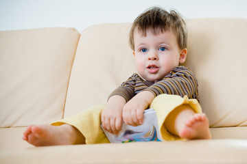 Little boy sitting on sofa with a book in hands