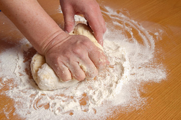 Hands of the baker knead dough in a flour