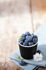 Blueberries in paper cup on wooden background