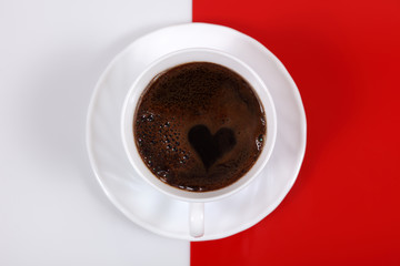 Kawa w białej filiżance z sercem, na biało czerwonym tle.
