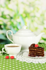 Teapot, cup of tea and delicious cake on natural background