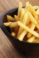 French fries in a wooden bowl, on a wooden background.