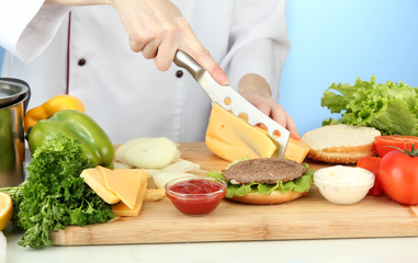 Female hands preparing cheeseburger, on blue background