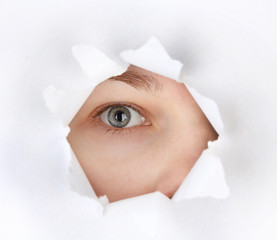 Female eye looking through hole in sheet of paper