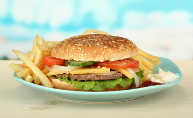 Tasty cheeseburger with fried potatoes, on bright background