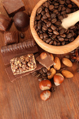 Chocolate sweets, mortar with coffee beans on wooden background