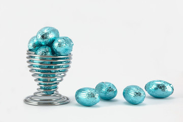 Blue foil Easter Eggs in wire eggcup and plain background.