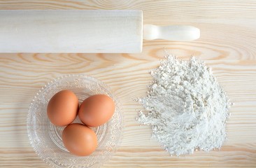 Flour, eggs and rolling pin on a wooden background