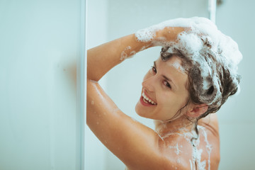 Smiling young woman washing head with shampoo