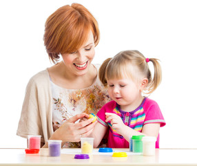 Happy child girl and mother sitting at table and playing with co
