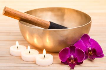 Klangschale mit brennenden Kerzen und Orchideenblüten