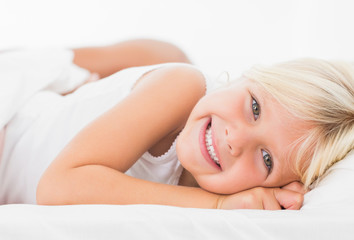 Obraz na płótnie Canvas Little girl lying on a bed and smiling