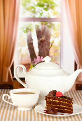 Teapot, cup of tea and delicious cake on window background