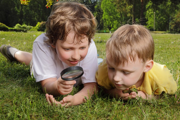 two boys with magnifying glass outdoors