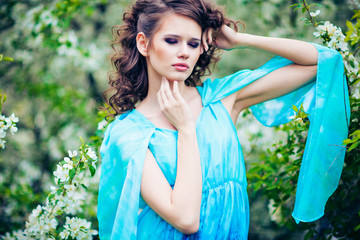 Beautiful woman in blue dress among blossom apple trees, fashion