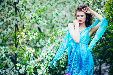 Beautiful woman in blue dress among blossom apple trees, fashion