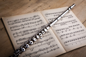 Naklejka premium Silver flute on an ancient music score background