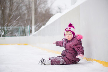 Fototapeta na wymiar Adorable girl skate on ice rink, seat on ice after fall
