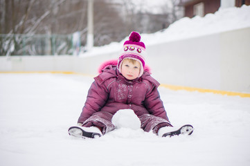 Adorable girl skate on ice rink, seat on ice covered with snow a