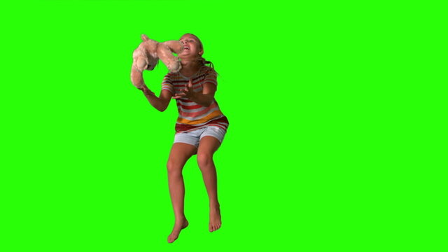 Girl jumping and catching teddy on green screen