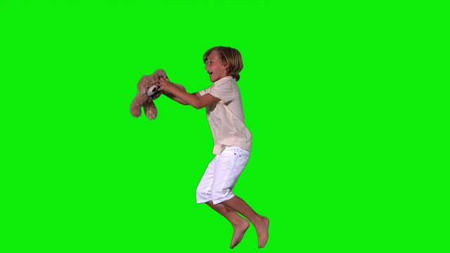 Cute boy jumping and catching teddy on green background