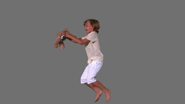 Cute boy jumping and catching teddy bear on grey background