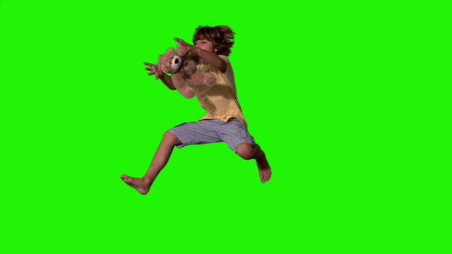 Little boy jumping up and catching teddy bear on green screen