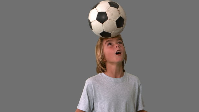 Young boy heading and kicking a football on grey background