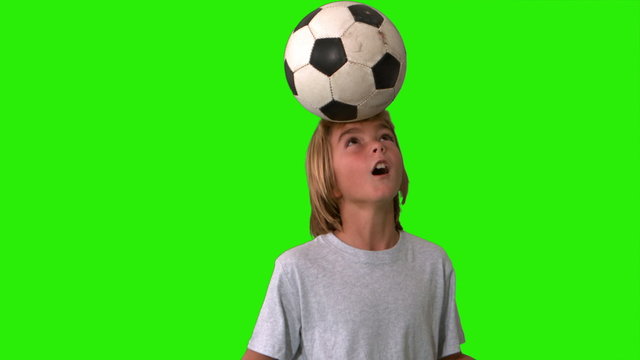 Young boy heading and kicking a football on green screen