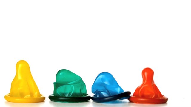 Four colourful condoms falling on white background