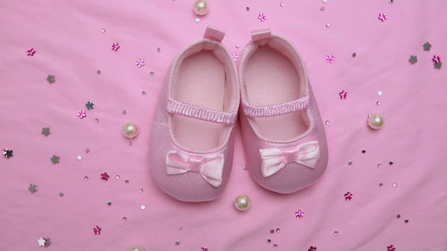 Pink baby booties on pink blanket with pearls