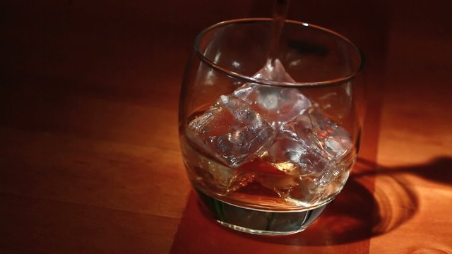 Tumbler of ice being filled with whiskey