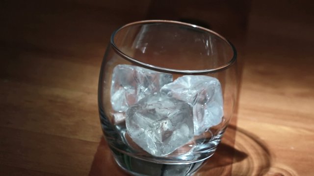 Hand putting ice into tumbler then pouring whiskey
