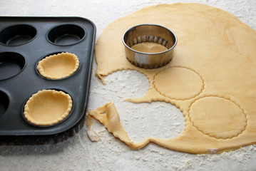 Pastry circles being cut and filling a bun tin to make jam tarts