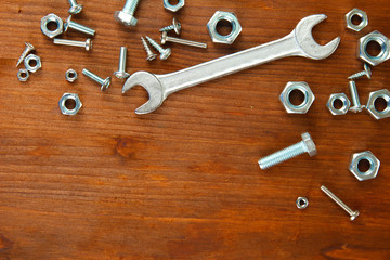 Bolts, screws, nuts and wrench on wooden table