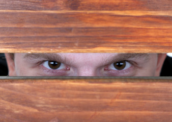 Man eyes looking through hole in wooden desk