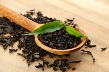 Dry tea with green leaves in wooden spoon, on wooden background
