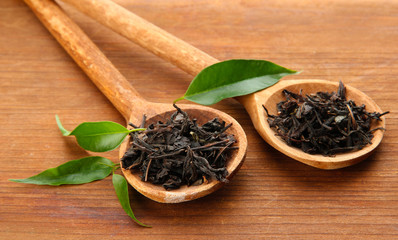 Dry tea with green leaves in wooden spoons, on wooden
