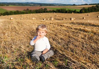Little boy eating German sausage on goden hay field