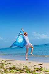 The young attractive woman jumping with a blue scarf in hands..