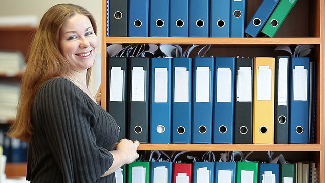 Woman standing behind bookshelves with file folders and smiling