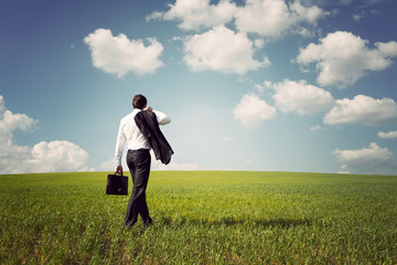 businessman in a suit walking on a spacious green field with a b
