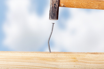 Crooked nail in the wooden board with a hammer